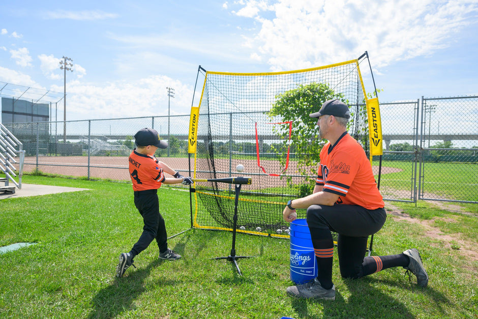 A Baseball player and his coach training with a batting tee and baseball net to improve his baseball skills