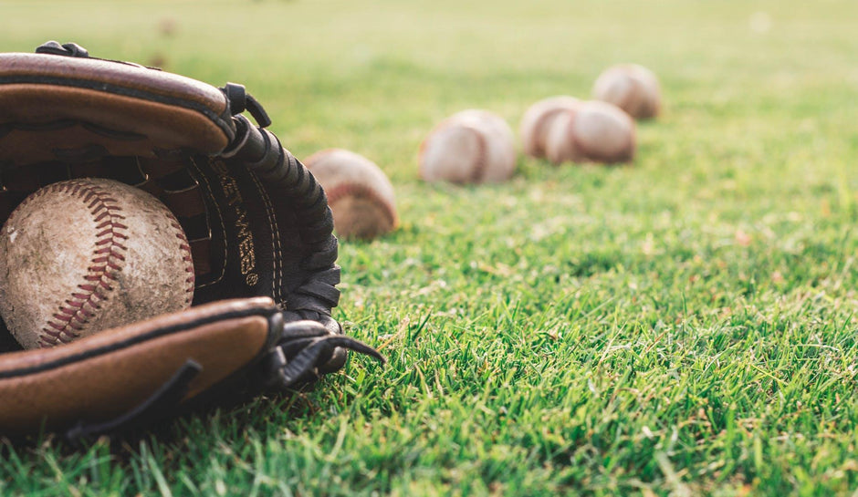 A baseball glove laying on the field with essential gear for baseball like baseballs surrounding it