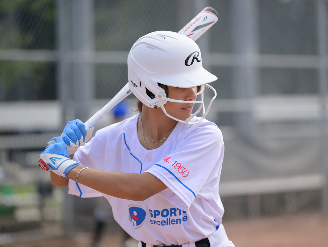 A fast pitch softball player at the plate with her fastpitch softball bat, batting gloves and baseball batting helmet on