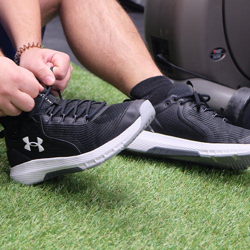 An athlete lacing up his Under Armour running shoes