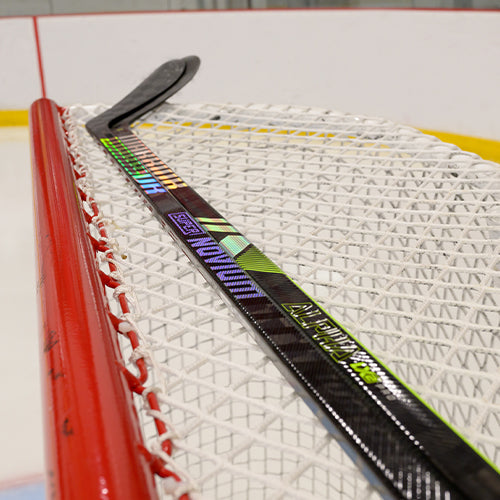 Two Warrior hockey sticks laying on top of a hockey net.